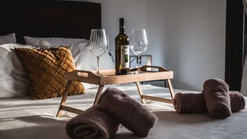 Ein ordentlich gemachtes Bett mit einem hölzernen Tablett, das eine Flasche und zwei Gläser trägt, ein braunes gestepptes Kopfkissen und aufgerollte Handtücher.