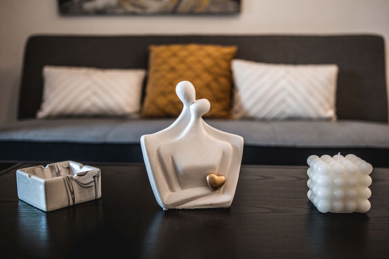 A modern living room with a dark sofa, two white cushions, a decorative white vase, and a small white object on a wooden table.