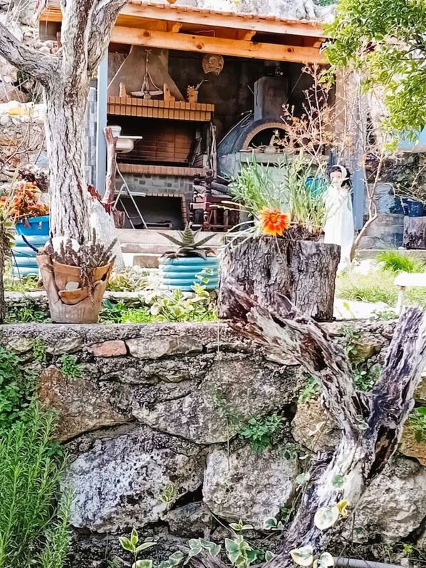 Un espacio al aire libre rústico con un muro de piedra, troncos de madera y plantas en macetas.