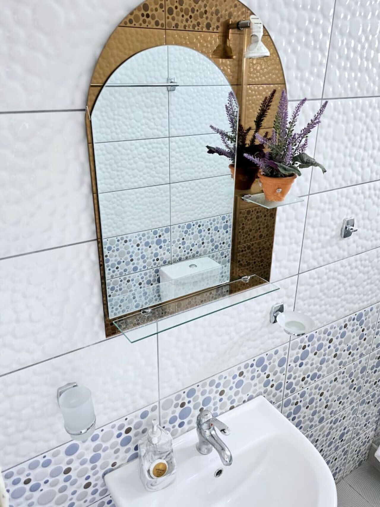 Un baño con un lavamanos blanco, un espejo con arco dorado y una planta en maceta.