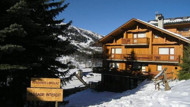 Un chalet en bois doté d’un balcon, entouré de montagnes enneigées.