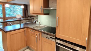 Une cuisine moderne avec des meubles en bois, des appareils en acier inoxydable et une fenêtre donnant sur la forêt.