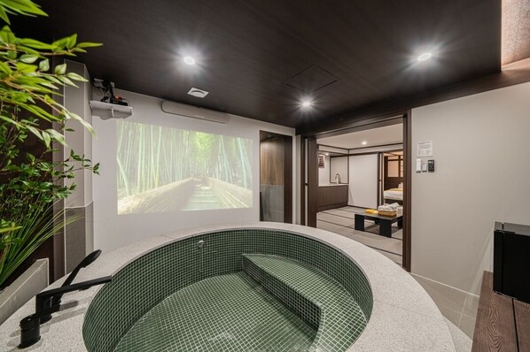 A modern spa room with a green-tiled hot tub, a projection screen displaying a forest scene, and a wooden bench. - Stay Passport Fukuoka Ryokan Daejeon Yuseong (Daejeon)