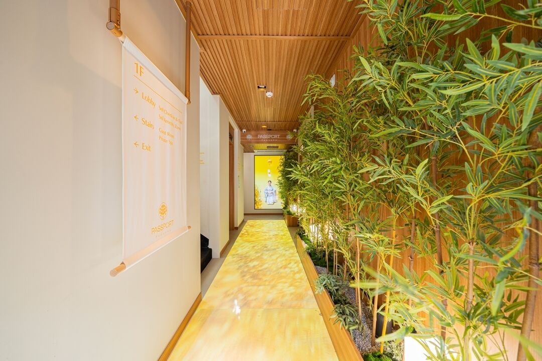 A hallway with directional signs, a wooden ceiling, and a plant-lined wall.