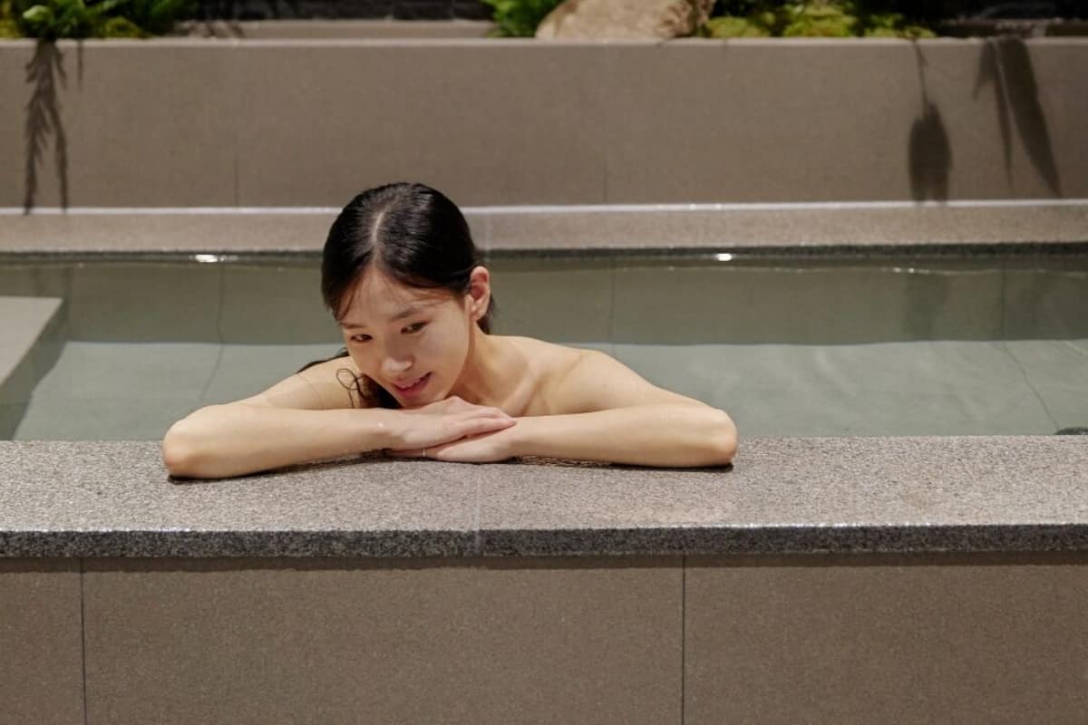 A person resting by a pool with a stone wall and greenery in the background.