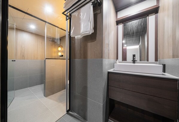 Un baño moderno con cabina de ducha de vidrio, un lavabo blanco y un mueble de tocador de madera oscura.