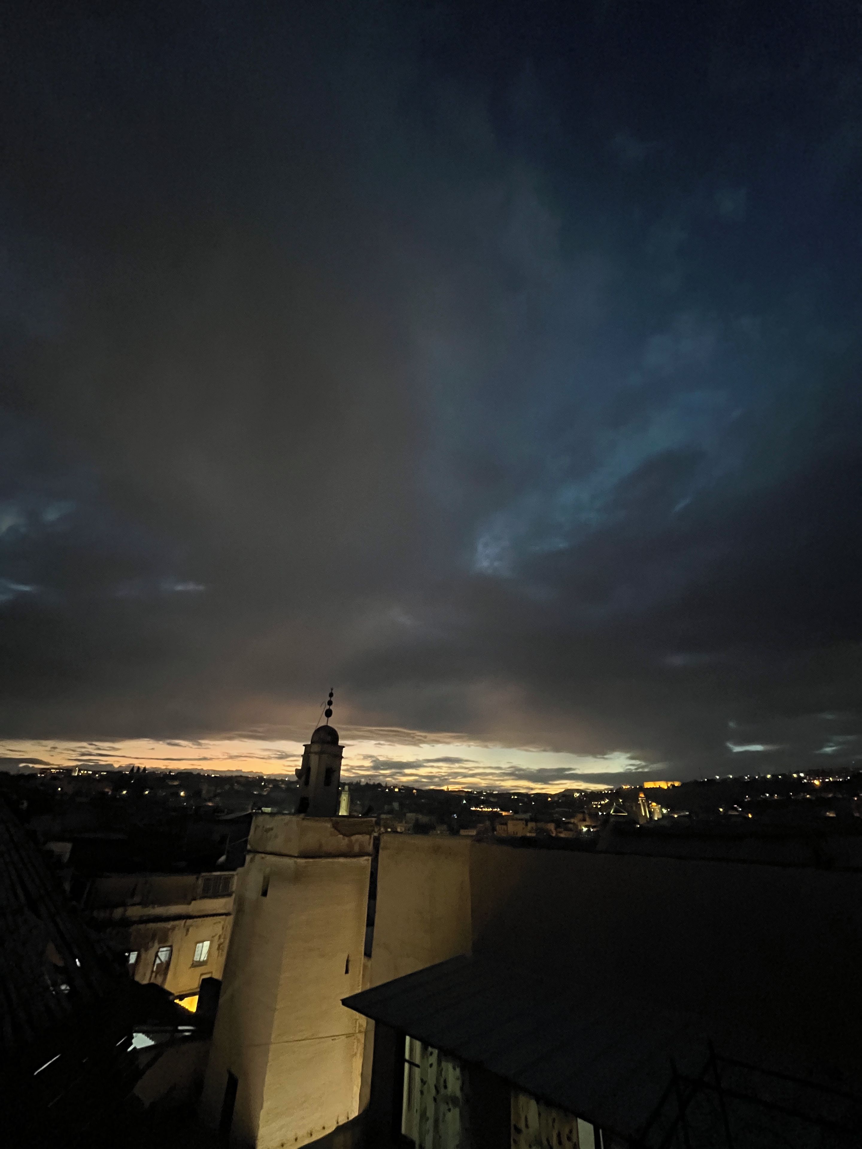 A cityscape at dusk with a prominent tower silhouetted against a cloudy sky.