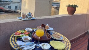Ein Tisch mit Essensanrichtung auf einem Balkon mit Blick auf eine Stadtlandschaft, einschließlich eines Turms und eines Topfpflanzes.
