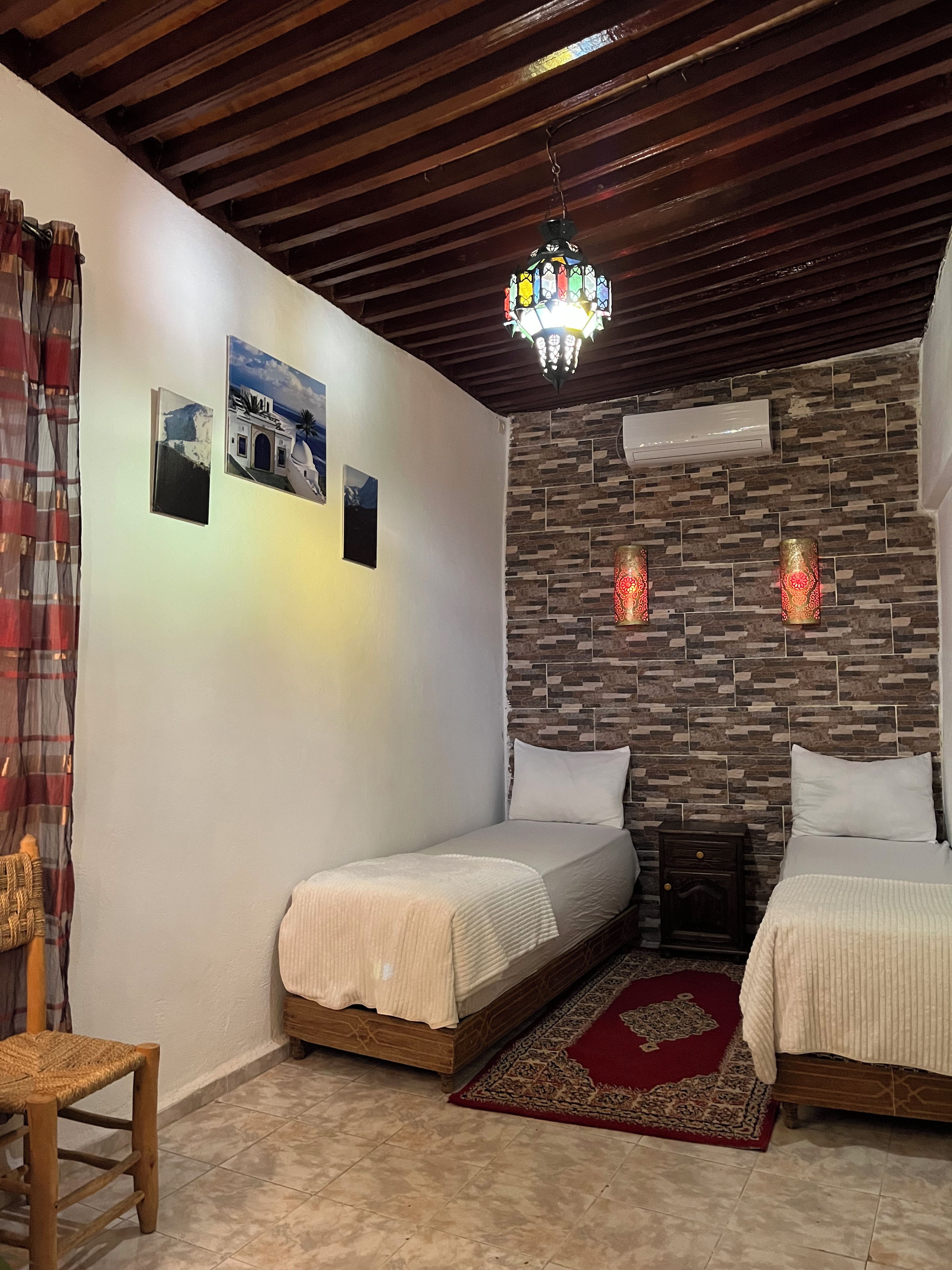 A bedroom with two beds, a wooden ceiling, a stone wall, and a chandelier.