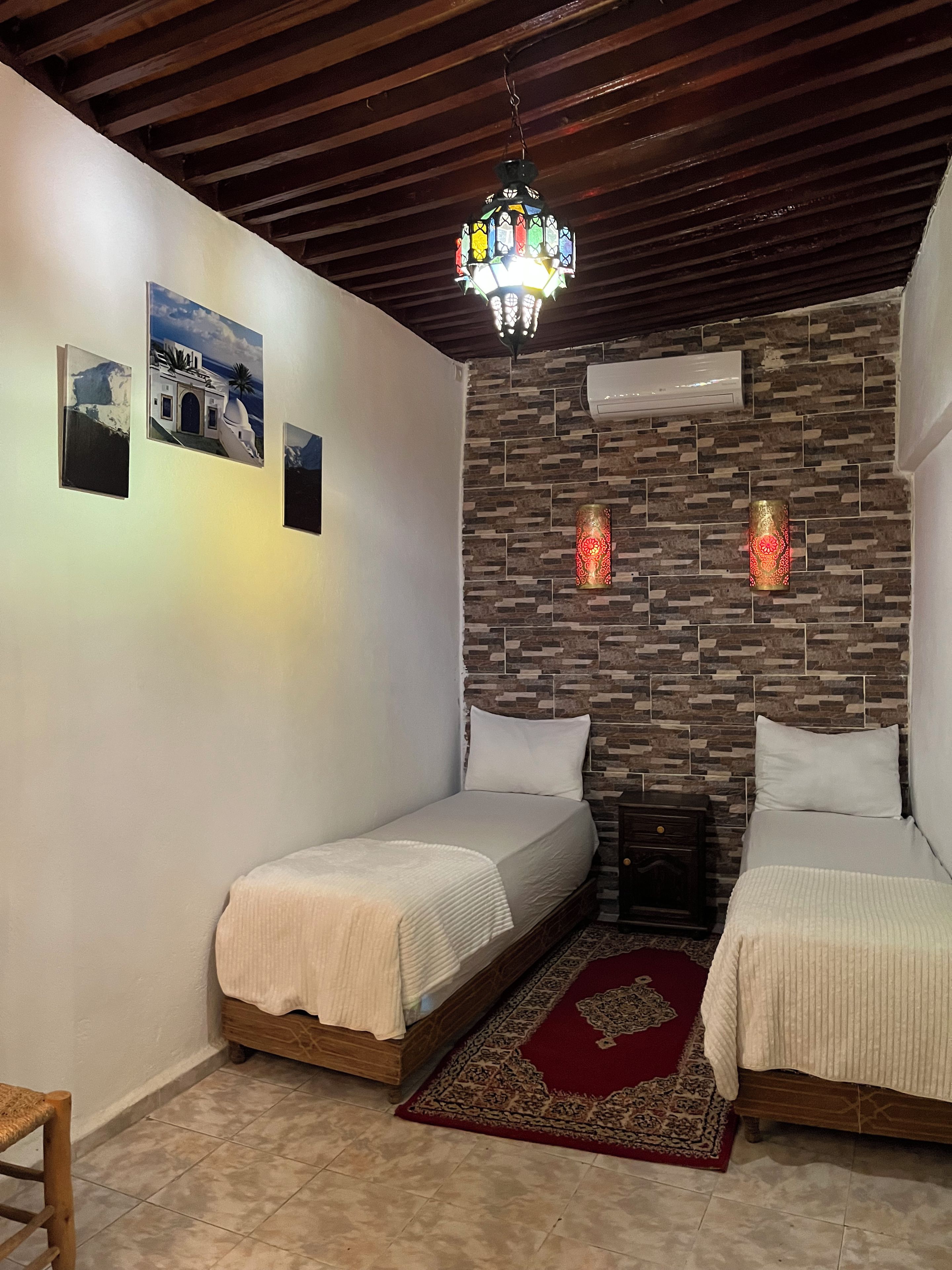 Una habitación con dos camas, un papel tapiz estampado, un candelabro y una alfombra roja.