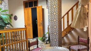 Ein traditionelles Interieur mit einer Holztreppe, Teppichen mit Muster und einem runden Tisch mit Stühlen.