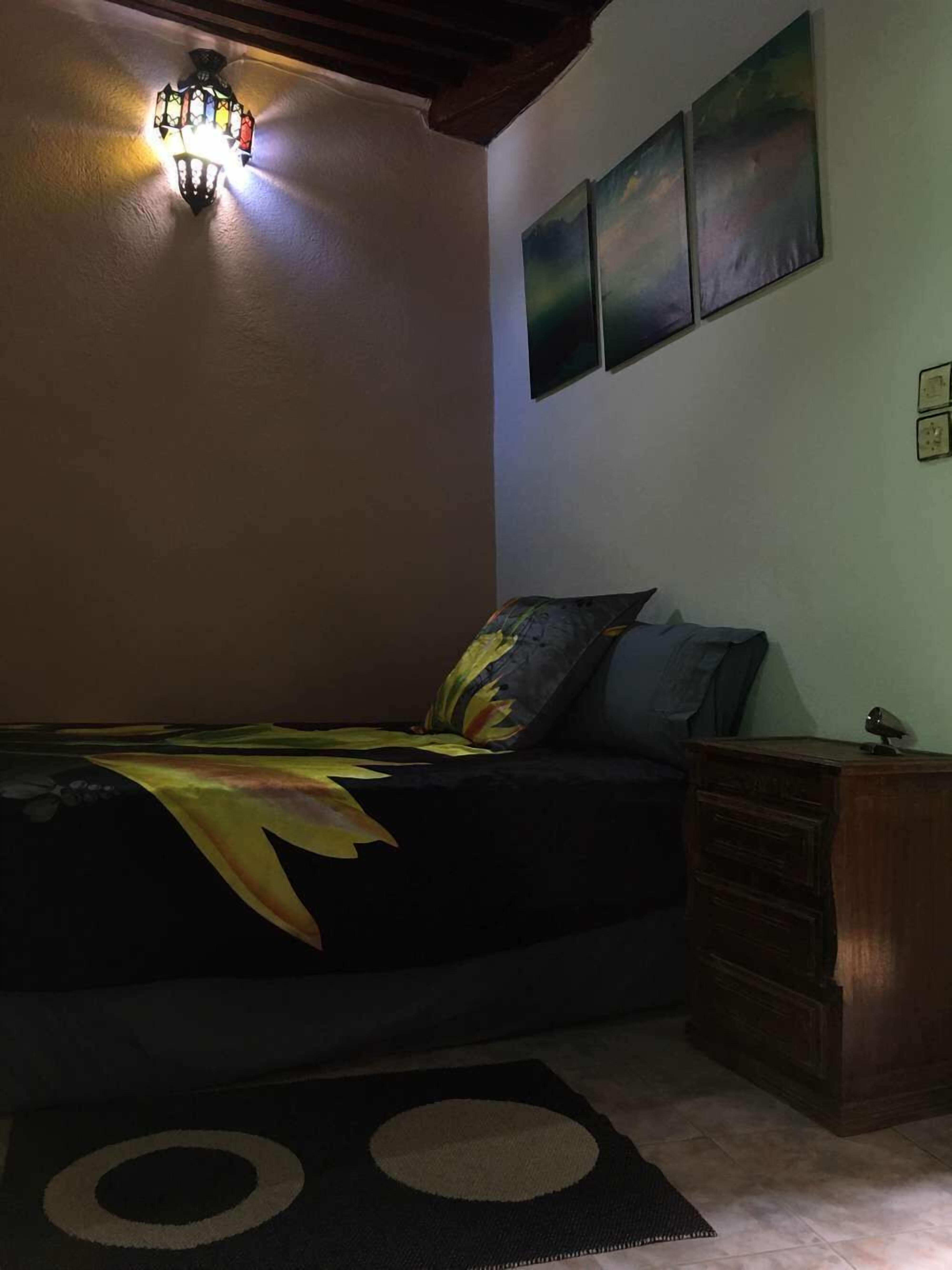Un dormitorio con cama, mesita de noche, lámpara y decoración en la pared.