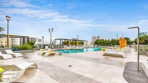 Zona de piscina en la azotea con sillas de descanso, una piscina y edificios modernos al fondo.