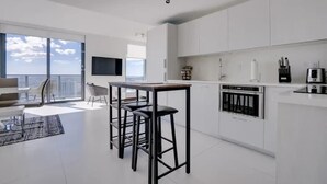 Una cocina moderna con armarios blancos, horno empotrado y un comedor con una mesa alta y taburetes.