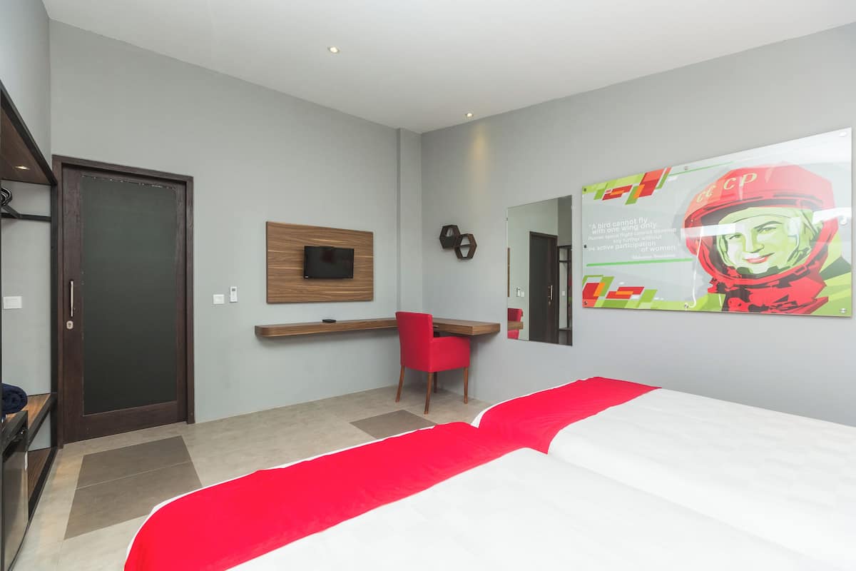 A hotel room with a bed, a desk, a chair, a TV, and a wall with a poster.