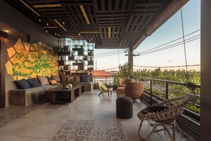 A modern outdoor lounge area with a geometric wall mural, comfortable seating, and a view of greenery. - 7Rooms Villa Seminyak (Seminyak)