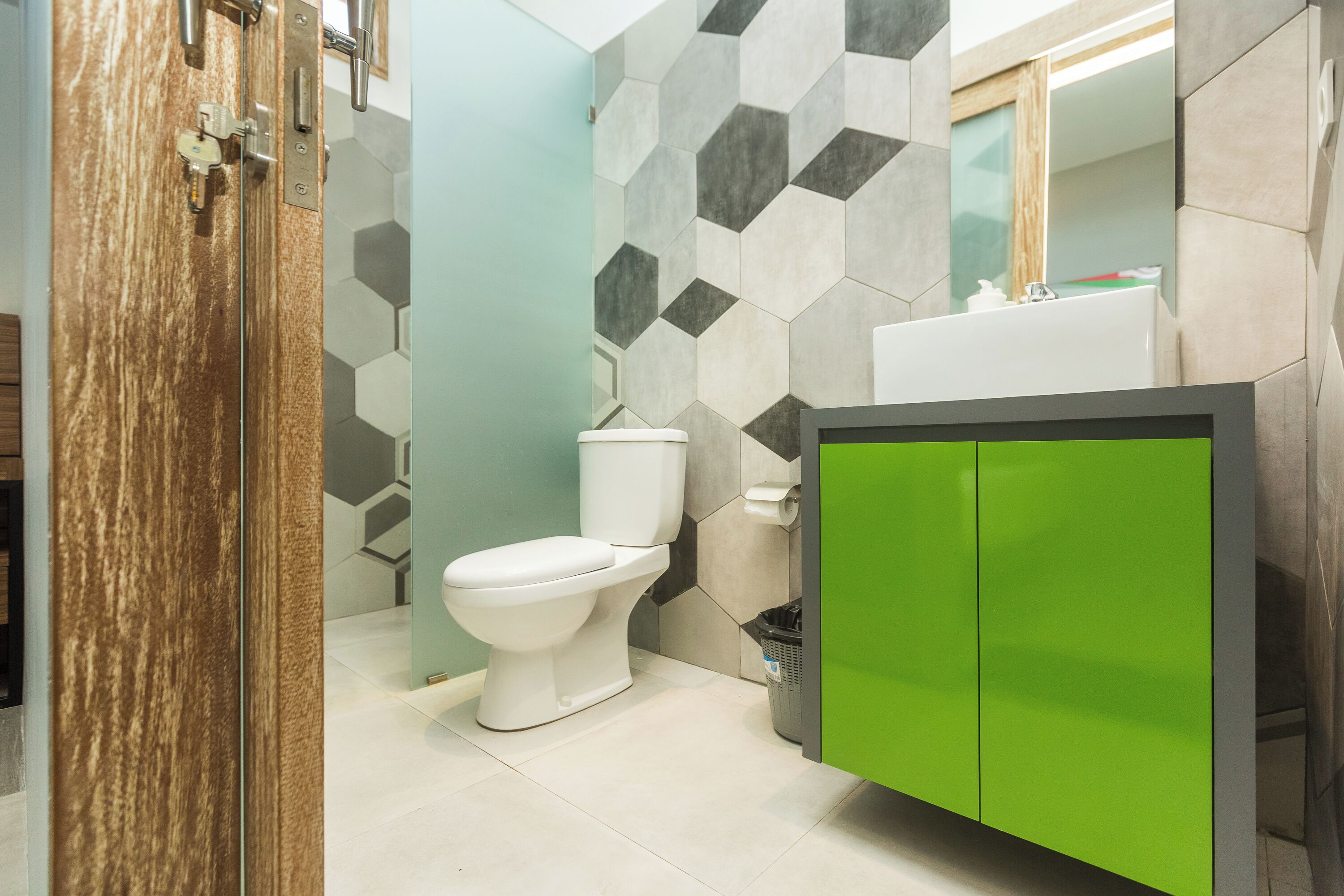 A modern bathroom with a white toilet, a green cabinet, and a hexagonal tile wall.