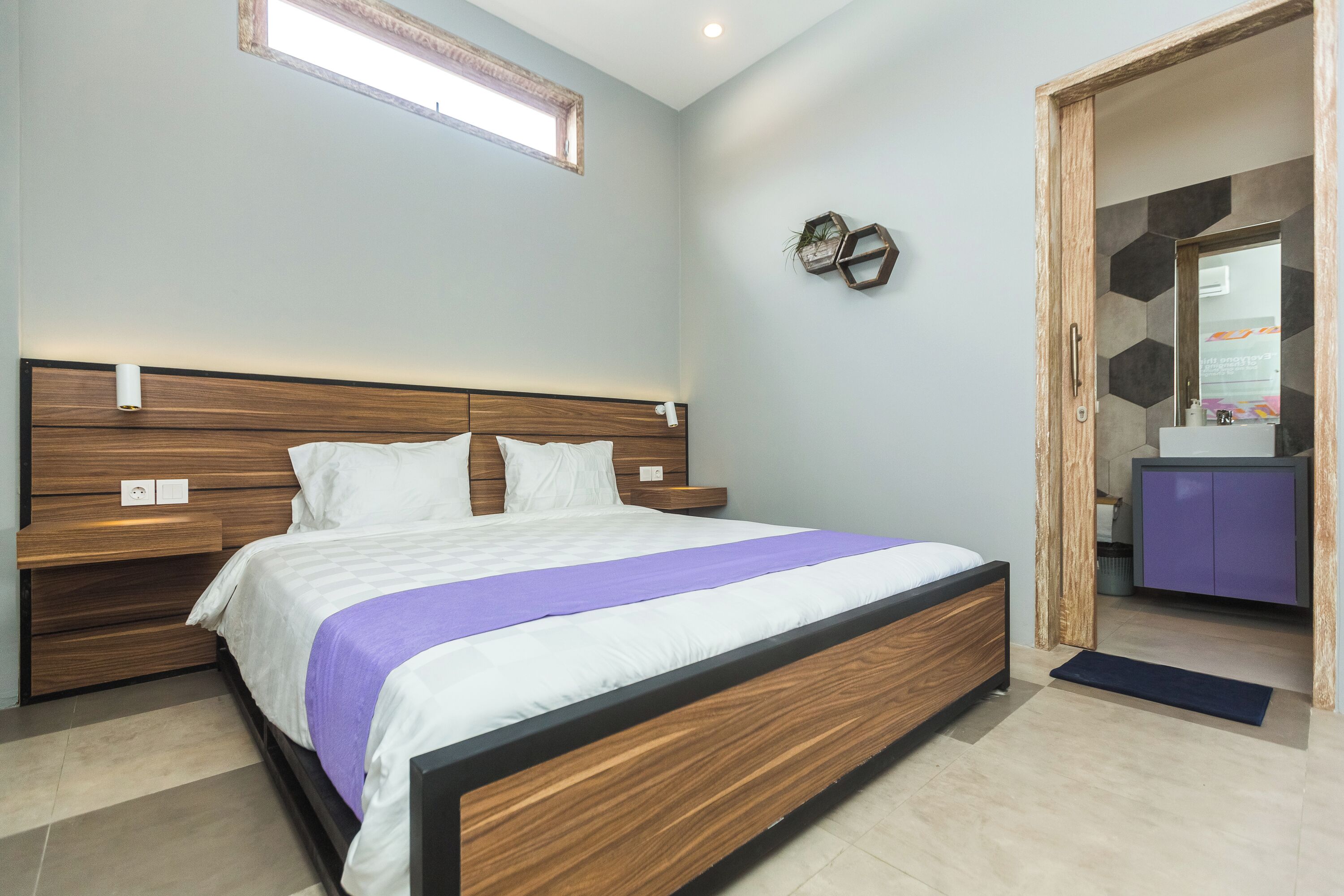Ein modernes Schlafzimmer mit einem Bett aus Holz, einem eingebauten Nachttisch und einem kleinen Badezimmer mit einem lila Schrank.