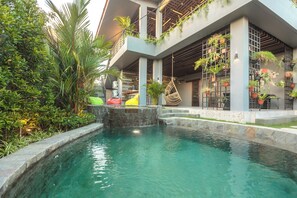 A pool area with a stone edge, surrounded by greenery and potted plants. - 7Rooms Villa Seminyak (Seminyak)