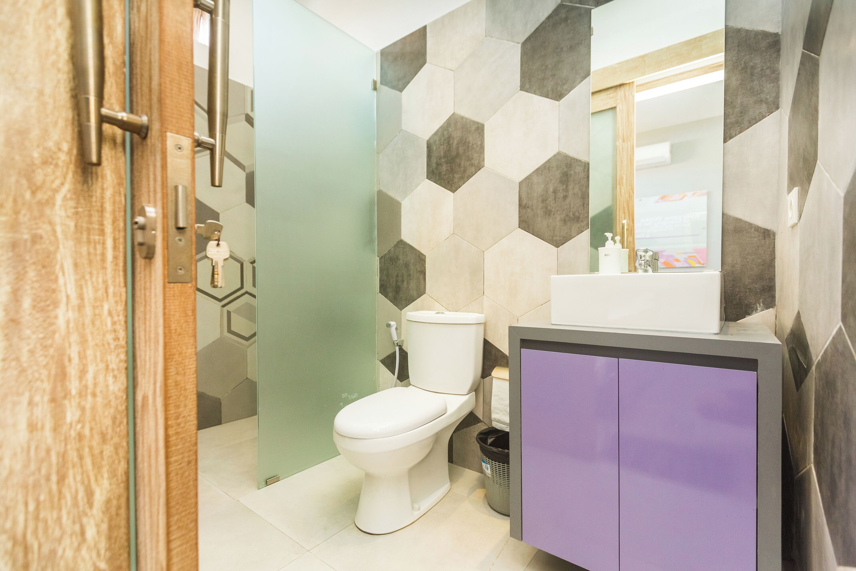 Une salle de bain moderne avec des toilettes blanches, un meuble violet et un miroir au-dessus du lavabo.