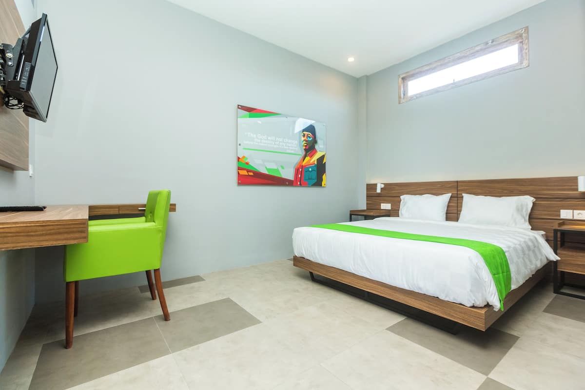 A hotel room with a bed, a desk with a chair, a television, and a wall-mounted artwork.