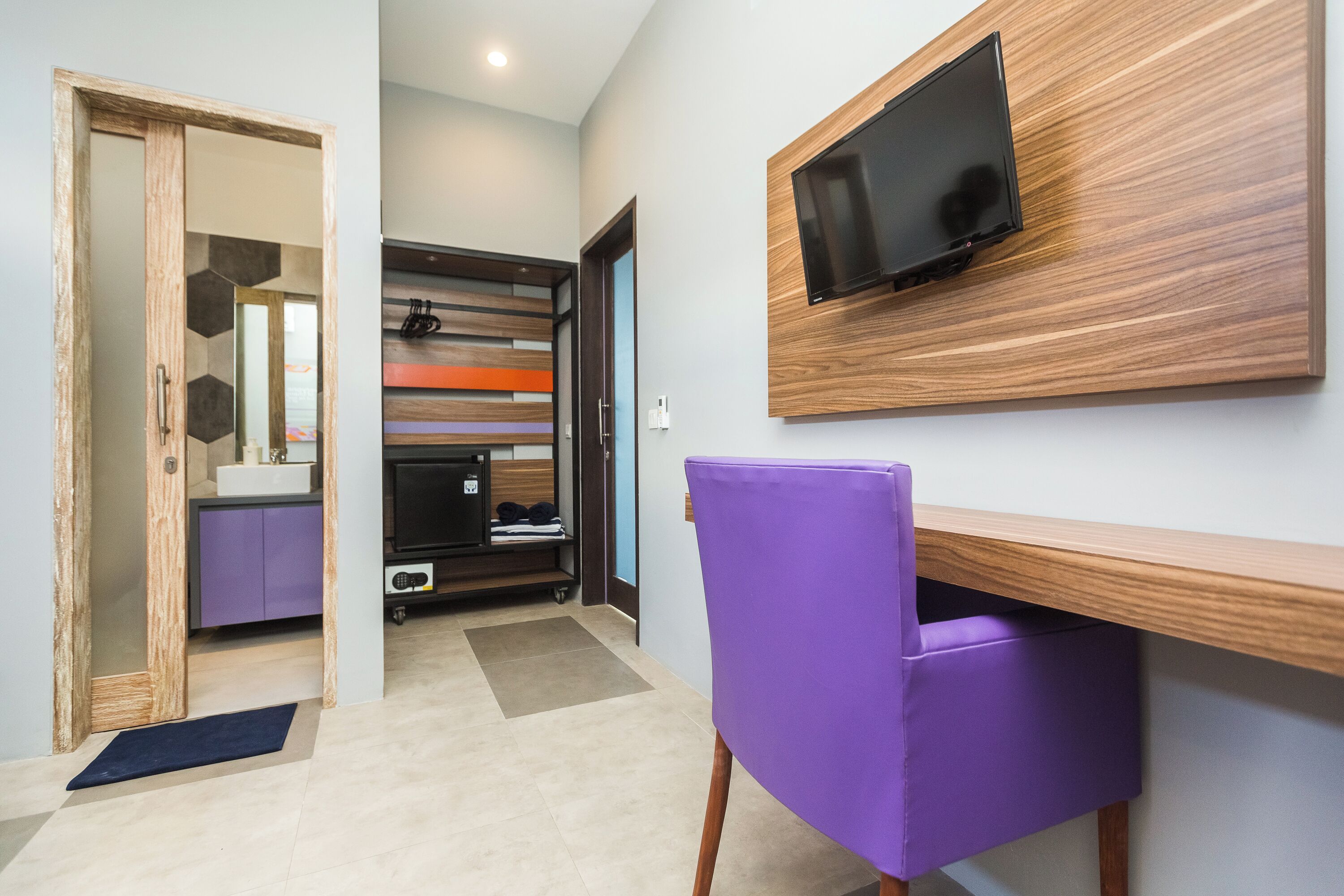A modern room with a wooden desk, purple chair, and a mounted TV.
