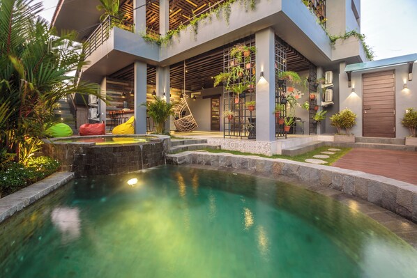 A modern building with a swimming pool, outdoor seating, and potted plants. - 7Rooms Villa Seminyak (Seminyak)