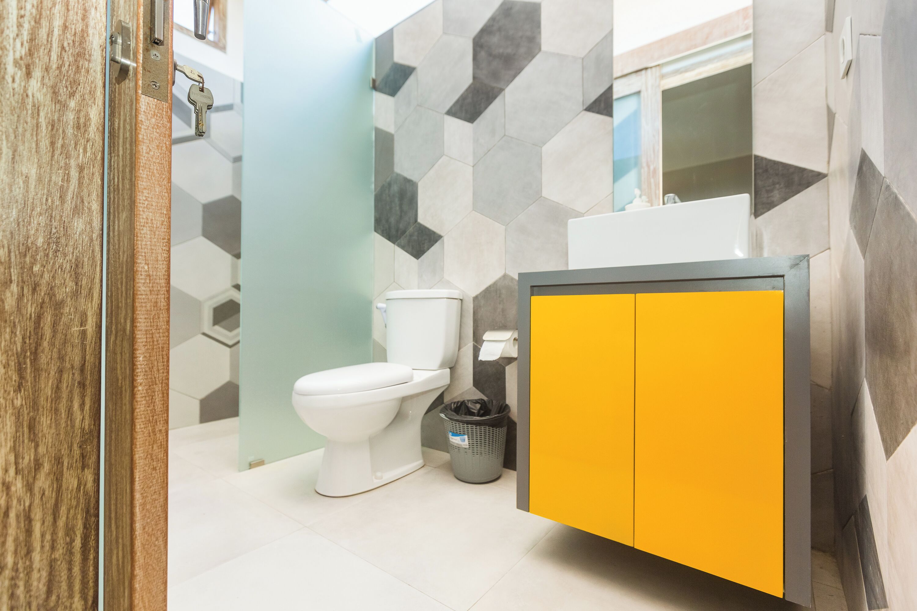 A bathroom with a white toilet, a yellow cabinet, and a grey trash bin.