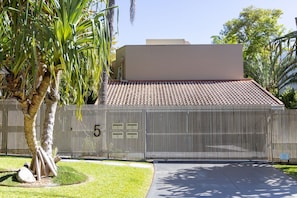 A gated entrance with a palm tree and a building with a tiled roof. - Coastal Serenity at Little Cove (Noosa)