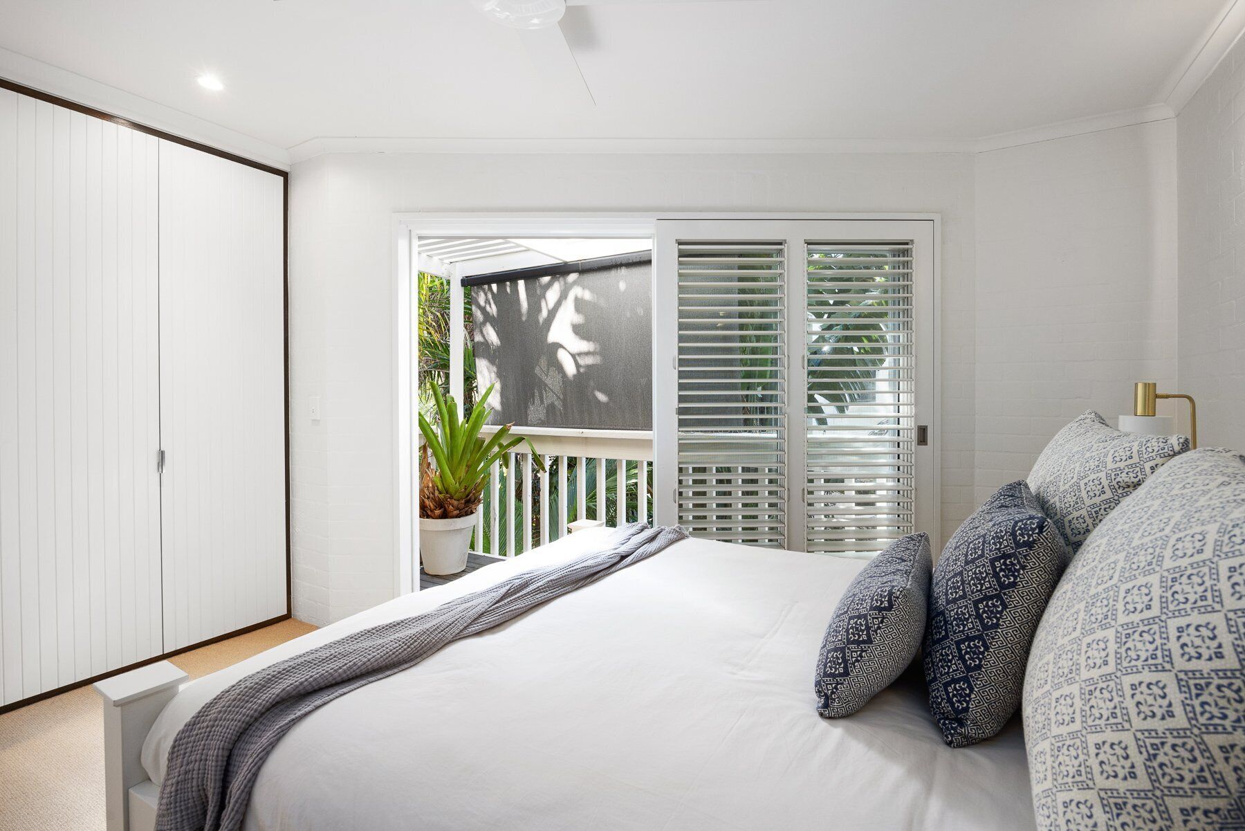 A bedroom with a bed, a potted plant, and a sliding door leading to a balcony.