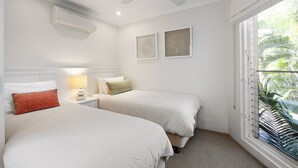 Ein Schlafzimmer mit zwei Betten, einem Deckenventilator, einer Klimaanlage und einem Fenster mit Jalousien.