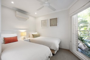Un dormitorio con dos camas, ventilador de techo, aire acondicionado y ventana con persianas.