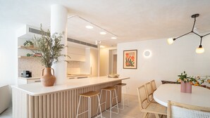 Una cocina moderna con una isla central, taburetes de bar y una mesa de comedor con sillas.