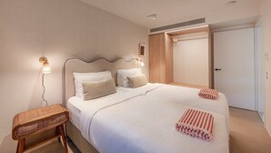 Una habitación de hotel con una cama grande, lámparas de noche, una mesita de madera y una puerta.