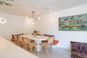 Un coin repas avec une table ronde, des chaises en bois, un lustre moderne et un tableau représentant une piscine.