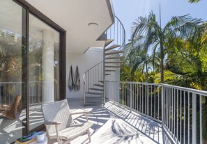 Un balcon avec une chaise blanche, une petite table et un livre. Un escalier en colimaçon y mène à un niveau supérieur.