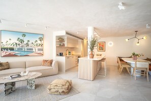 Un salon moderne avec un canapé, une table basse et un tableau représentant un paysage tropical.
