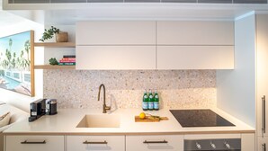 A modern kitchen with a white countertop, a built-in sink, a backsplash of speckled tiles, and a range hood above the stove. - Little Cove Luxe - Naousa 10 (Noosa)