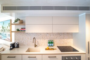 Une cuisine moderne avec un plan de travail blanc, un évier encastré, un pare-feu en carreaux à motifs et une hotte aspirante au-dessus de la cuisinière.