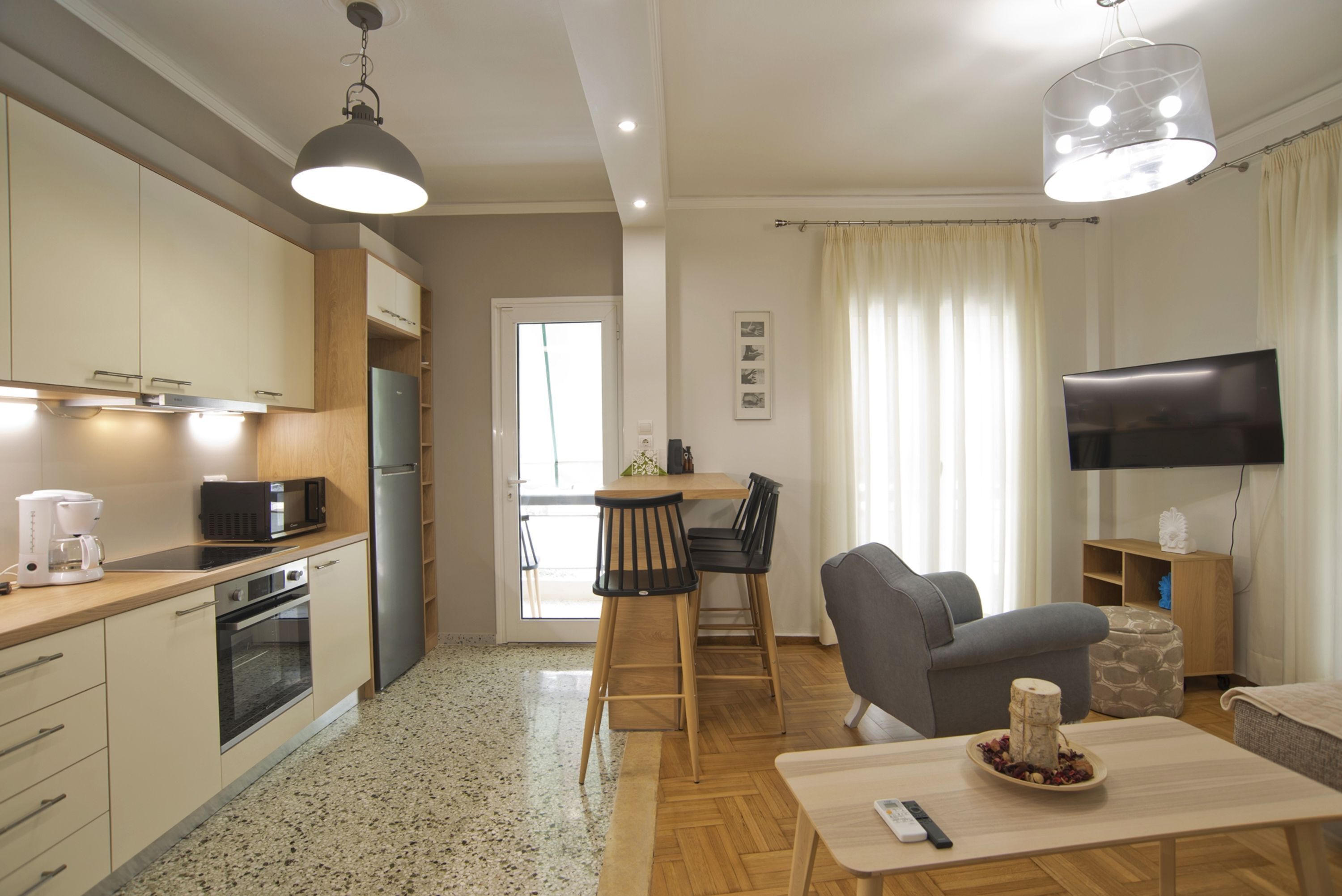 A modern kitchen with a microwave, coffee maker, and oven. There is a dining area with a table and chairs, and a TV mounted on the wall.