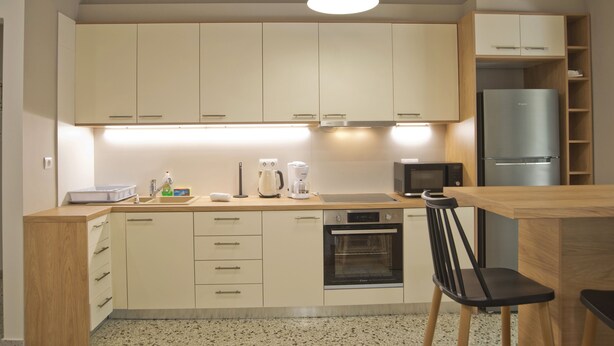 A compact kitchen with light-colored cabinets, a built-in oven, a microwave, and a refrigerator. - Fabi s Place in Kipseli (Athens)