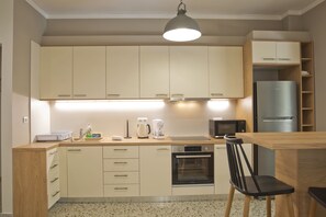 A compact kitchen with light-colored cabinets, a built-in oven, a microwave, and a refrigerator. - Fabi s Place in Kipseli (Athens)