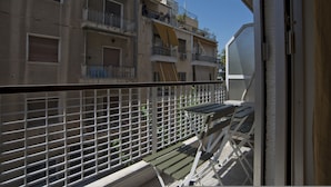 Un balcon doté d’une rambarde en métal, d’un banc vert et offrant une vue sur un immeuble à plusieurs étages, lui aussi pourvu de balcons et de fenêtres.