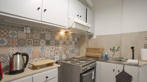 Une cuisine équipée d’une cuisinière, d’un four et de divers appareils électroménagers. On y trouve une planche à découper en bois et une bouilloire sur le plan de travail.