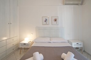 A hotel room with a bed, two bedside tables, a wardrobe, and two wall-mounted air conditioning units.