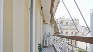 Un balcone stretto con pavimento piastrellato, ringhiera in metallo e vista sui palazzi vicini.