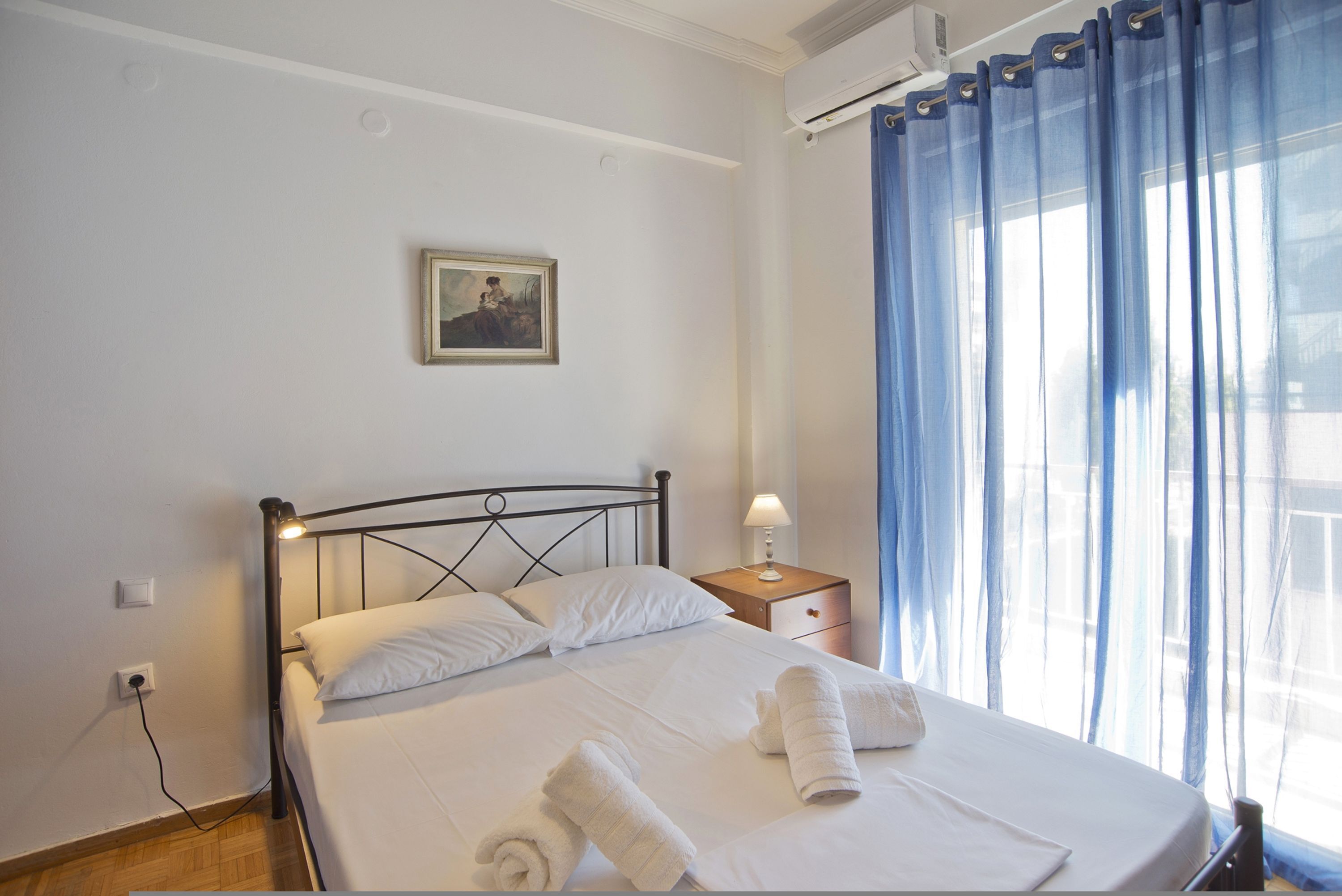 A neatly made bed with white linens and towels, a bedside lamp, and a small bedside table.