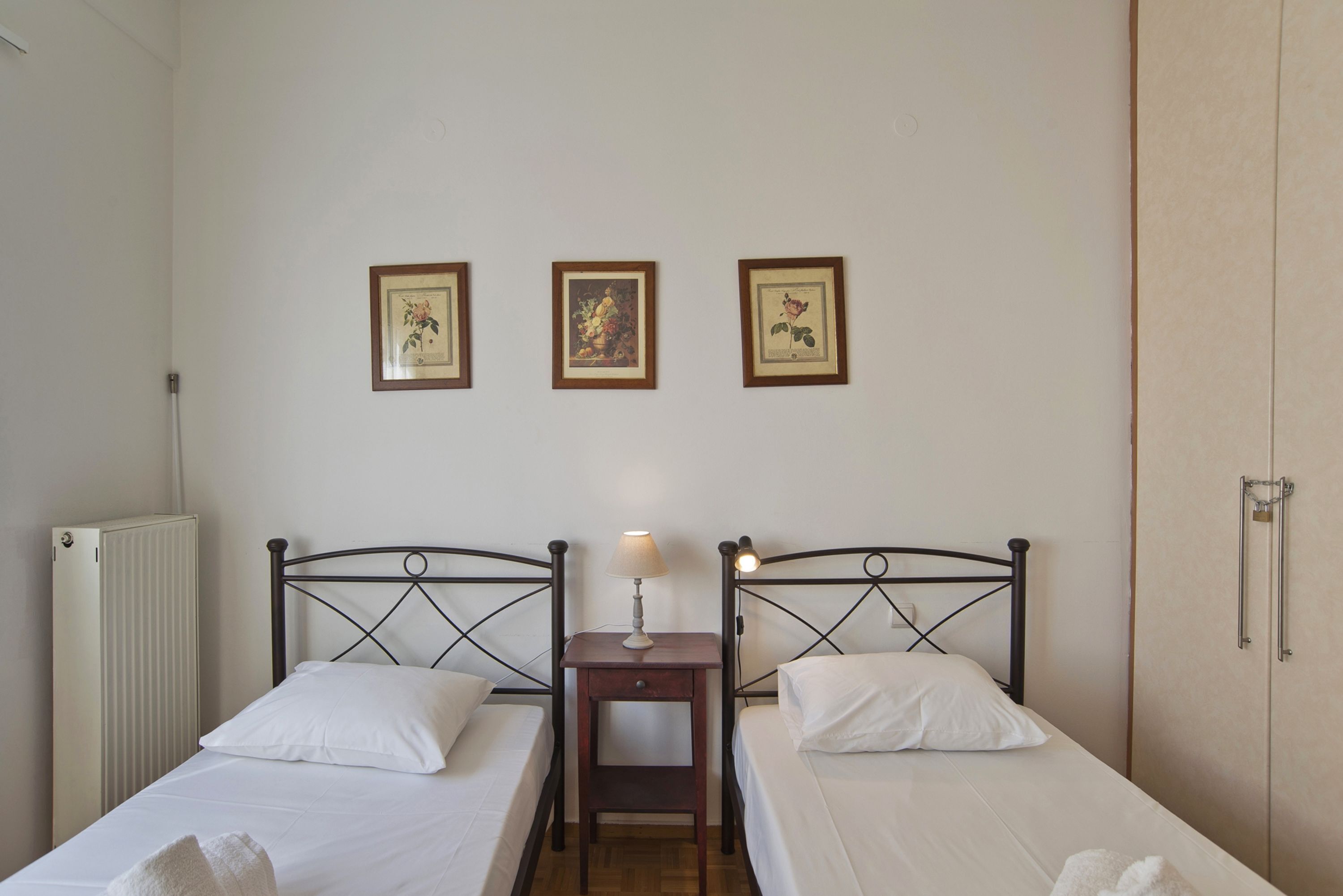 Een kamer met twee bedden, een nachtkastje met een lamp en drie afbeeldingen in lijsten aan de muur.