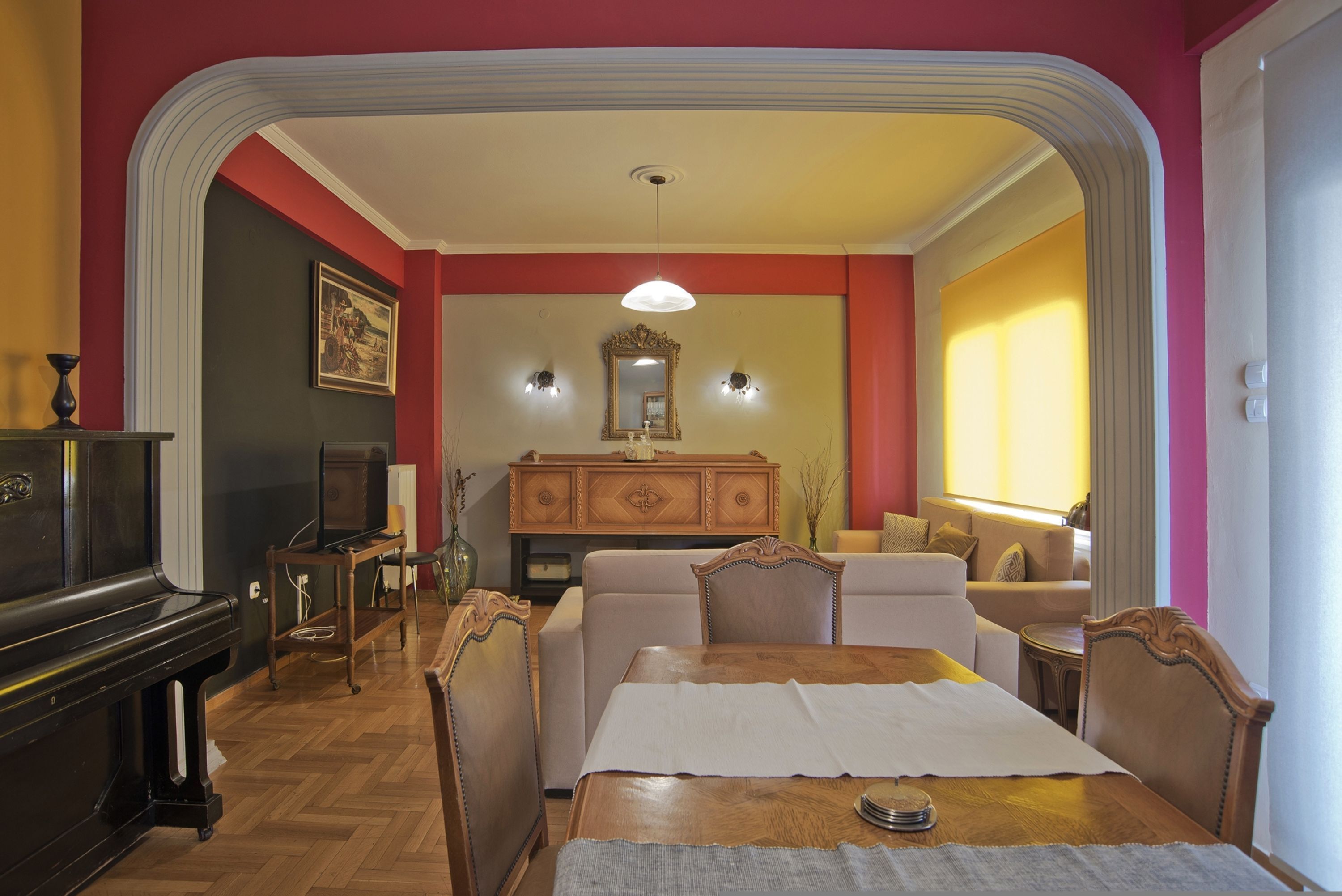 Un comedor con una mesa de madera, sillas y un sofá. Hay un piano y un televisor en la habitación.