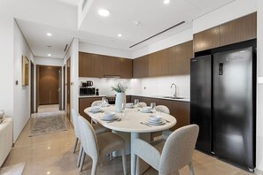 Une cuisine moderne avec un coin repas, comprenant un grand réfrigérateur noir, des meubles de rangement en bois et une table ronde pour quatre personnes.